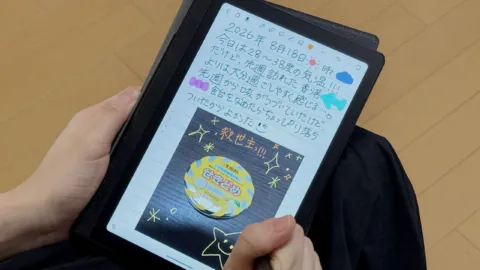 Huion Note Eを手に持って文字を描いている